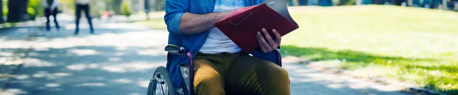 Person in wheelchair reading a book on a university campus path, highlighting the importance of adapting university facilities for disabled students to ensure equal access to education and resources.