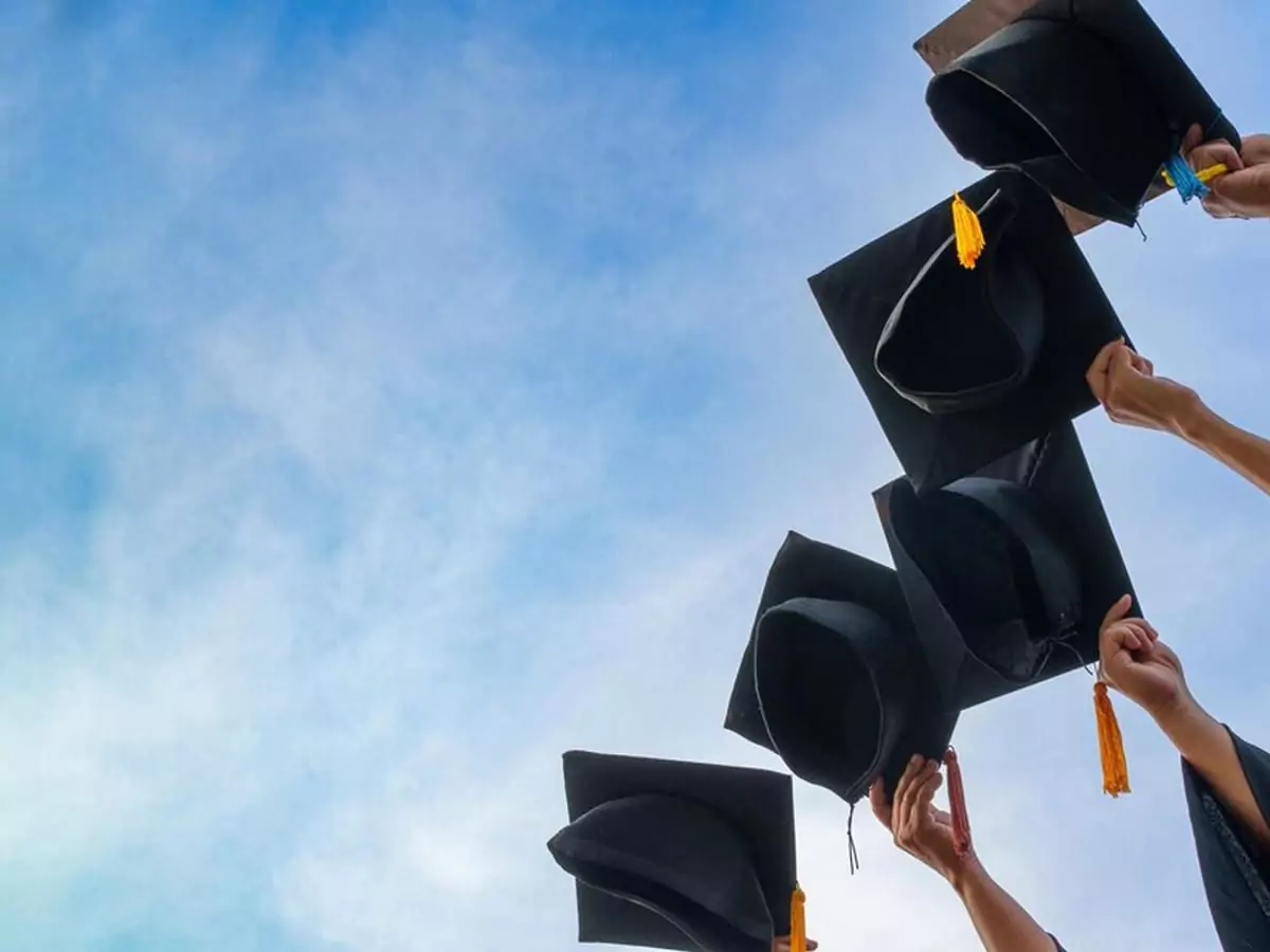 hands holding graduation caps with the sky as the background