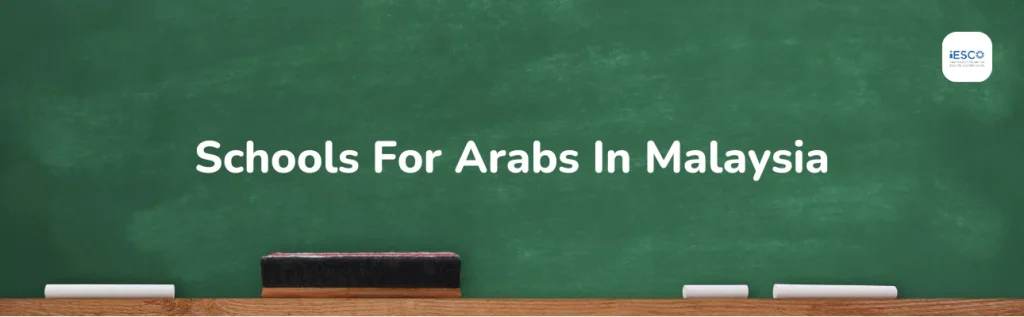 a green chalkboard with the text "Schools For Arabs In Malaysia" written in white. At the bottom of the chalkboard, there is a wooden ledge with a blackboard eraser and a few pieces of chalk. In the top right corner.